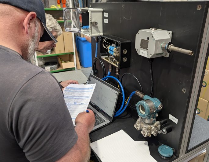 Two technicians inspecting hazardous area equipment with a laptop and documentation in a workshop setting.